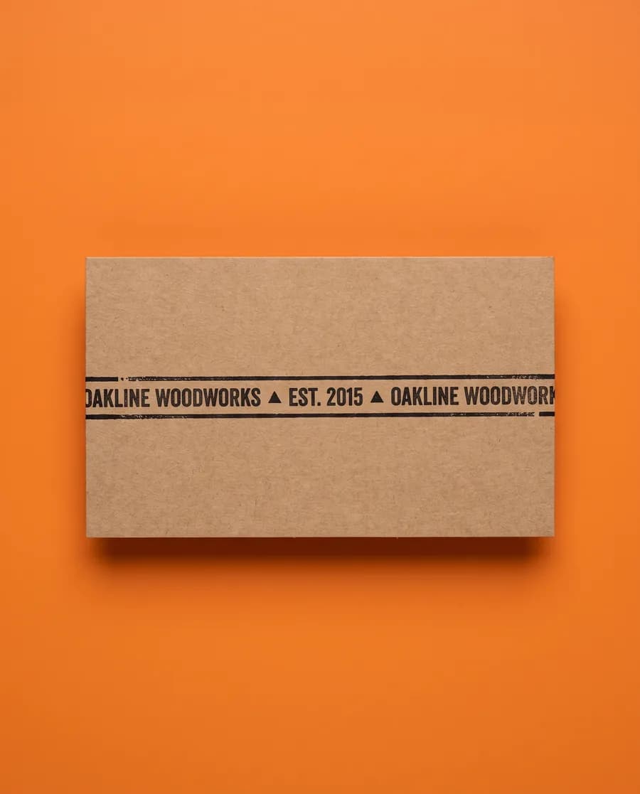 Kraft proof card on orange: Oakline Woodworks, est. 2015, repeating on a single 14 mm line, printed with a Rolly L