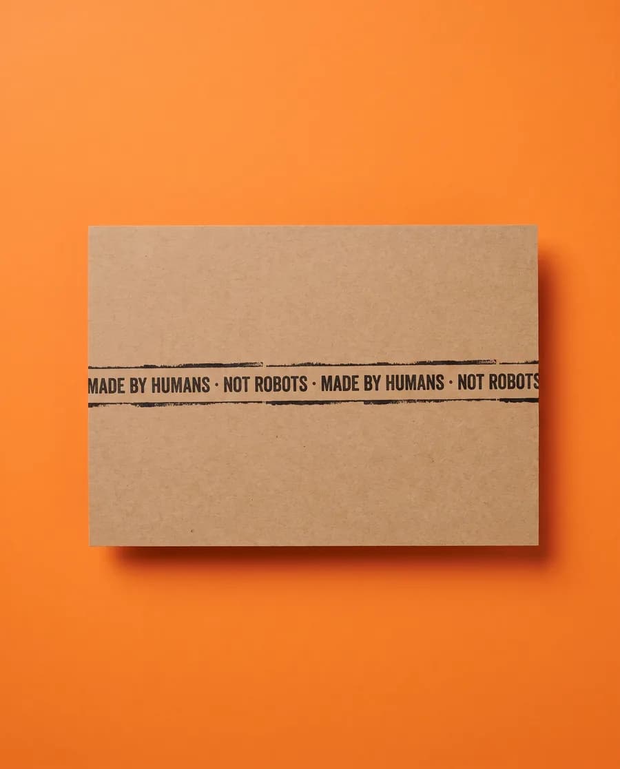 Kraft proof card on orange: Made by humans, not robots, repeating on a single 14 mm line, printed with a Rolly L